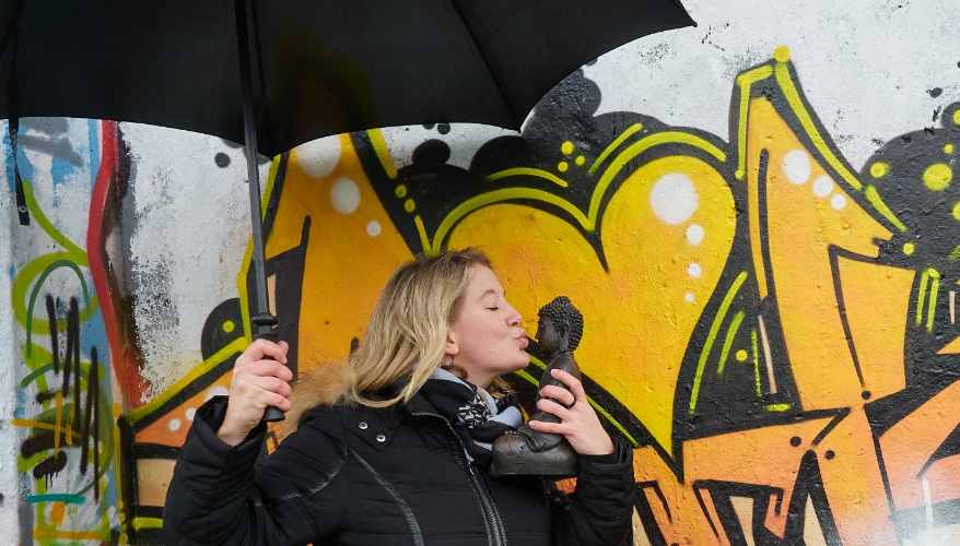 Monika mit schwarzem Schirm vor Graffitiwand und küsst Buddha